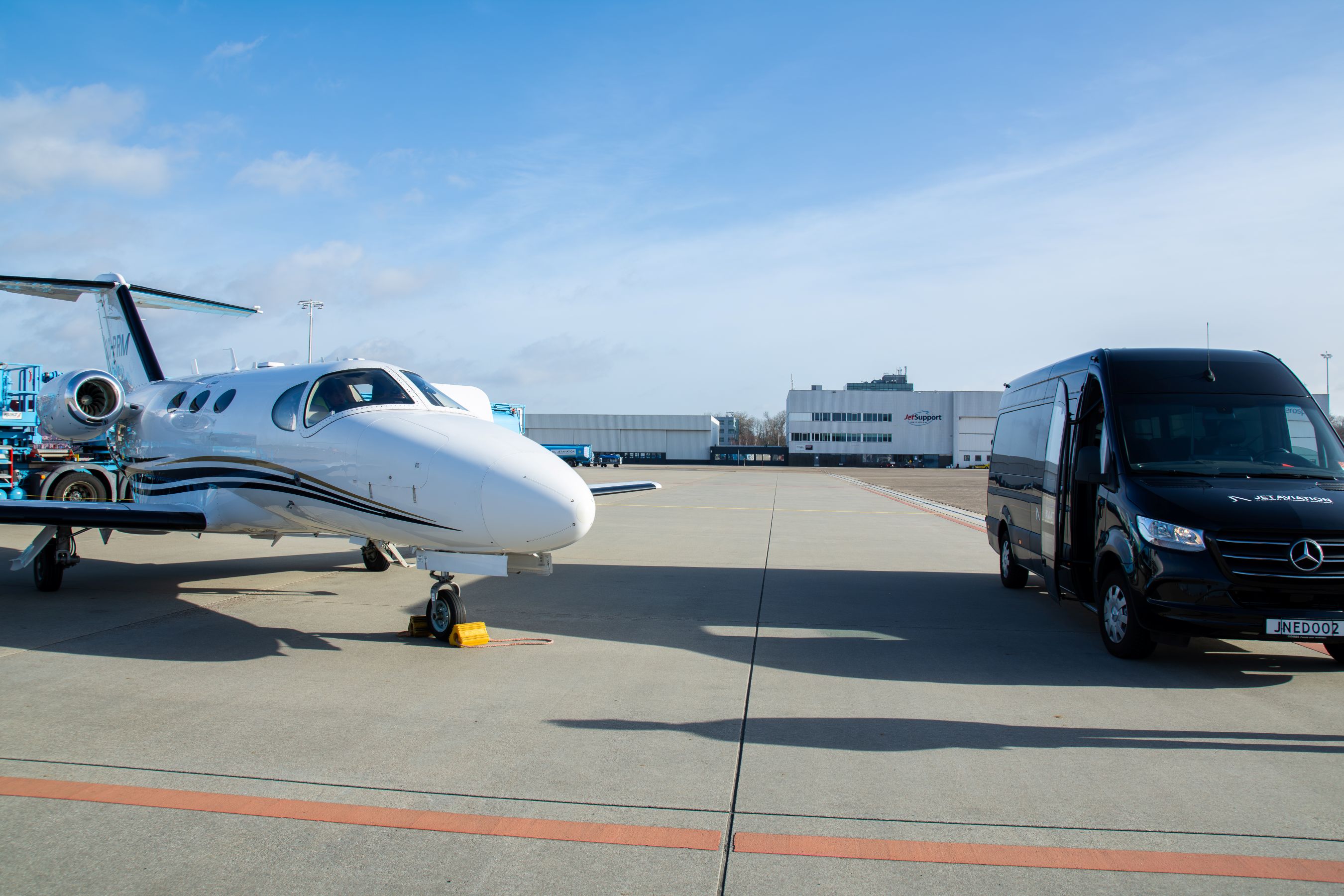 Cessna Citation Mustang geparkeerd op Amsterdam Schiphol Airport, met een FBO‑auto die op het platform klaarstaat voor de passagier.